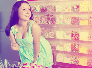 Obraz na płótnie Canvas Smiling girl sucking lollypop in store