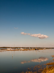 beautiful estuary scene with blue sky moored boats, masts, and reflection of cloud in water surface