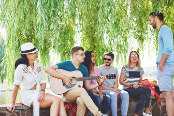 Group of happy friends with guitar. While one of them is playing guitar and others are giving him a round of applause