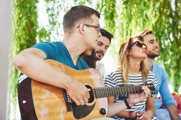 Group of happy friends with guitar. While one of them is playing guitar and others are giving him a...