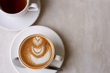 Hot coffee with flower shape latte art in white cup on marble desk with copy space
