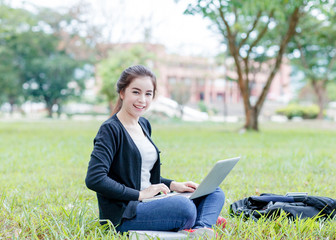 female student sitting on the green field with laptop computer