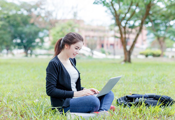female student sitting on the green field with laptop computer