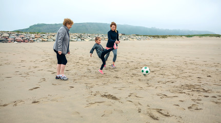 Three generations female playing soccer on the beach in autumn