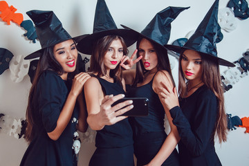 Obraz premium Women in witch halloween costumes standing and make selfie on white background.