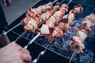 Grilled kebab cooking on metal skewers (grill). Roasted meat cooked at barbecue with smoke. Close up BBQ fresh pork meat chop slices. Traditional eastern dish, shish kebab