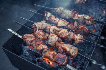 Grilled kebab cooking on metal skewers (grill). Roasted meat cooked at barbecue with smoke. Close up BBQ fresh pork meat chop slices. Traditional eastern dish, shish kebab