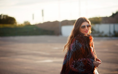 elegant brunette in sunglasses and mink coat walking in the street