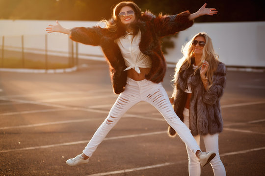 two glamorous girlfriends in mink coats and sunglasses walking on the street