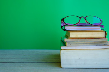 Stack of books and eye glasses on top on the wooden table and green background, teacher's day concept.