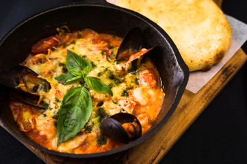 freshly cooked seafood clams with cheese in tomato sauce in metal pan on cutting board