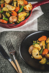 Plate and Skillet with  fried seasonal autumn vegetables (zucchini, potatoes, carrots, beans), on black stone table copy space top view