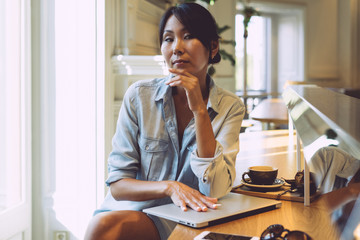 Entrepreneur female is working in a modern coworking space with a smartphone and a portable computer connected to wi-fi. Asian woman closed the laptop when finished her working day.