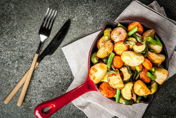 Plate and Skillet with  fried seasonal autumn vegetables (zucchini, potatoes, carrots, beans), on black stone table copy space top view