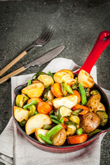 Skillet with  fried seasonal autumn vegetables (zucchini, potatoes, carrots, beans), on black stone table copy space top view