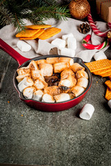 Indoor s’mores, baked s’mores dip in a cast iron skillet pan with graham crackers., dark grey table, copy space, with christmas tree and decorations