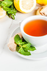 Cup of ginger tea with lemon,fresh mint and honey, on white marble table, copy space