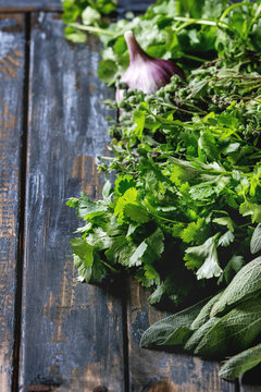 Variety of fresh organic herbs coriander, sage, oregano with garlic over old wooden plank background. Close up with space.