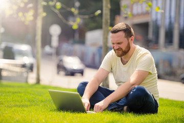Obraz premium young man with a laptop on the lawn, working outdoors in the city
