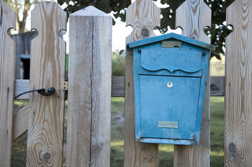 Blue decorative old retro style mailbox attached to a wooden fence