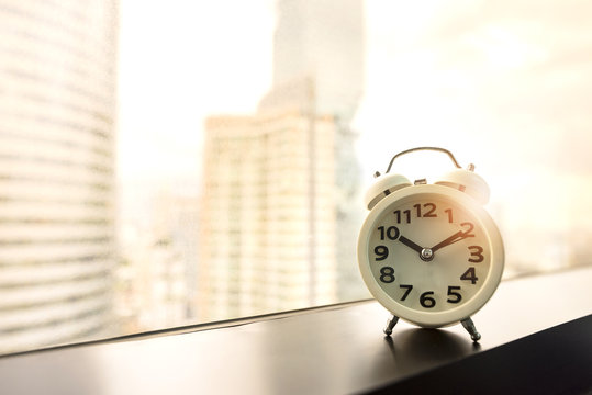 Timetable work concept, White alarm clock on window in modern office at early morning time