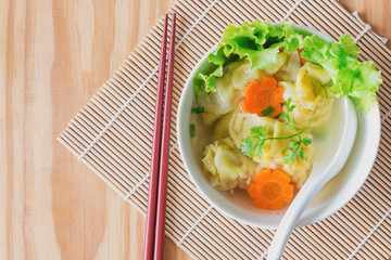 Homemade minced pork and shrimp wonton soup in white bowl on wood table in top view flat lay.Delicious wonton in clear soup for breakfast or lunch or dinner.Wonton or dumpling is popular Chinese food.