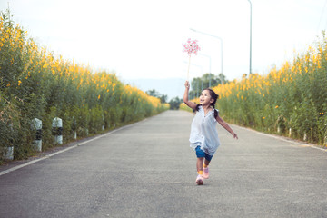 Fototapeta premium Cute asian little child girl playing with wind turbine and running on the road in the garden in vintage color tone