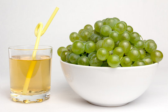 A glass with fresh grape juice and a white bowl full of green grapes.
