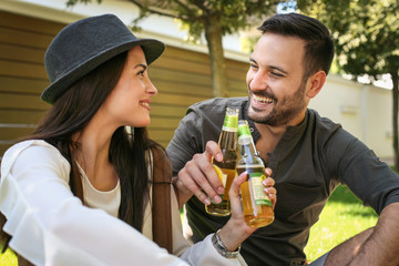 Young couple sitting in park and holding bottle of drink. Couple toast with bottle of drink.