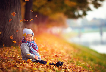 adorable happy girl playing with fallen leaves in autumn park