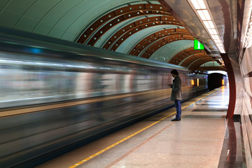 Lonely young man with smartphone shot from profile at subway station with blurry moving train in background.