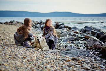 Two little twin sisters on a walk with dog on the beach.