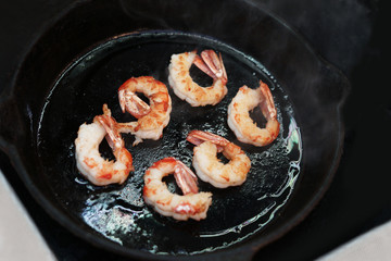 Big king prawns are fried in a black frying pan.