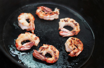 Big king prawns are fried in a black frying pan.