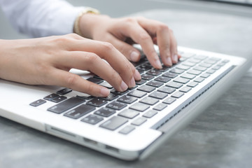 Close up hands of an employee is using a computer notebook by typing on keyboard at the desk.