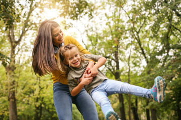 Mother and daughter playing together. Mother turns her daughter into a circle in the meadow.