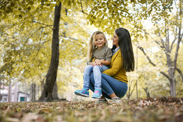 Mother and daughter outdoors in a meadow. Little girl sitting on mother lap.
