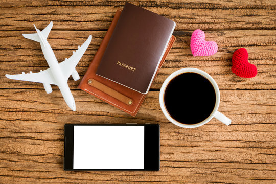 Passport and black coffee and a wallet and a plane model and red heart and smartphone with copy space for ad text put on the wood texture for travel planning and advertising business concept.