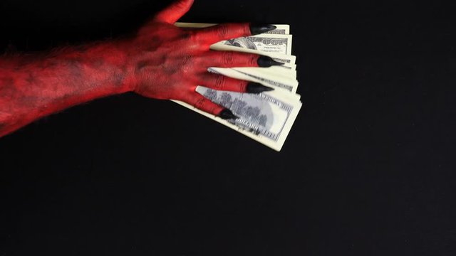 Devil's hand is playing with a pile of money.