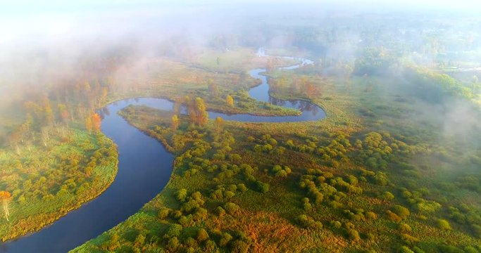 Scenic river winding through Autumn wilderness landscape in sunlight and fog, aerial flyover.