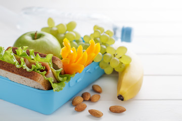 School lunch box with sandwich, apple, sweet pepper, grape and bottle of water on white wooden table.