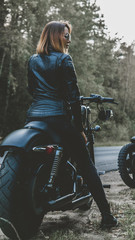 Fototapeta na wymiar Outdoor lifestyle portrait of sexy biker girl wearing leather jacket sits on a modern motorcycle, forest road