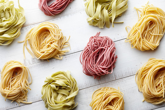 Several types of italian pasta on white wooden background, top view