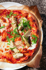 whole pizza in plate on natural stone with artichoke and arugula .