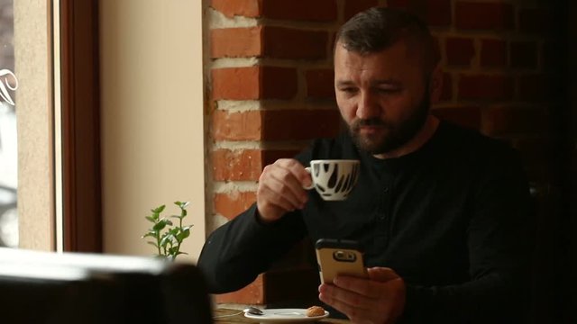 Handsome man texting messages on smartphone and drinking coffee
