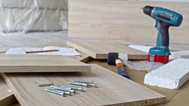 PAN with close up of disassembled wooden furniture, slabs of polystyrene beads, drill and screws lying on floor
