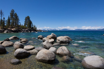 Fototapeta na wymiar Pine trees, rocks, and snowy mountain at Sand Harbor, Lake Tahoe, Nevada on a sunny winter day