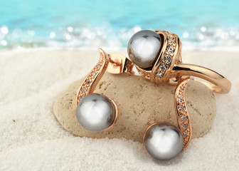 Jewelry set with black pearls on sand beach background, copy space