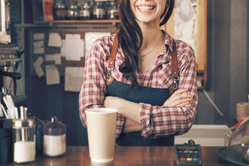Young female barista smiling, while serving a coffee at the counter - obrazy, fototapety, plakaty