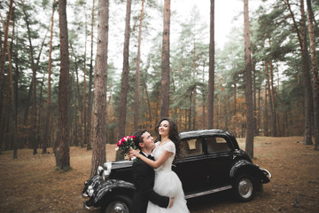 Naklejka premium Stylish wedding couple, bride, groom kissing and hugging near retro car in autumn